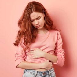 Woman touching her tummy suffering from menstrual pain in the pink background