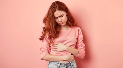 Woman touching her tummy suffering from menstrual pain in the pink background